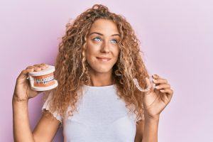 woman holding clear aligner and model teeth with braces